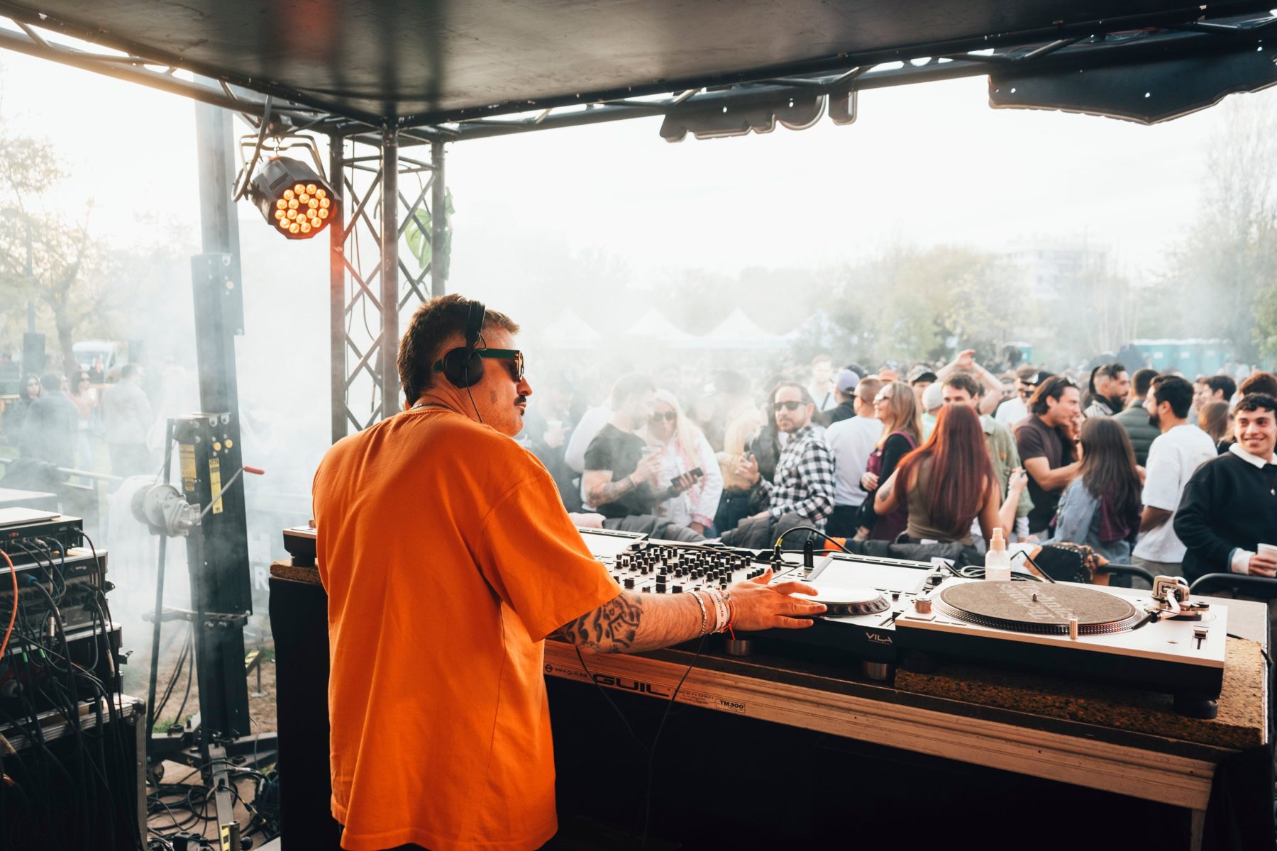 DJ con camiseta naranja pinchando vinilos frente al público