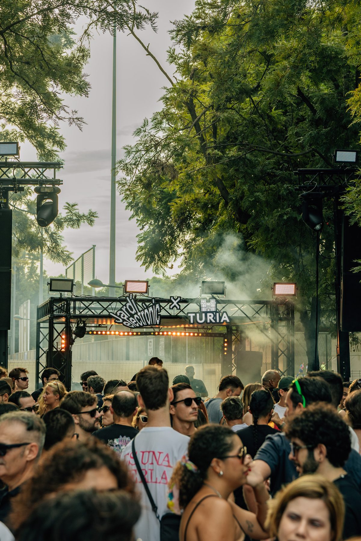 Público frente al escenario entre árboles y humo